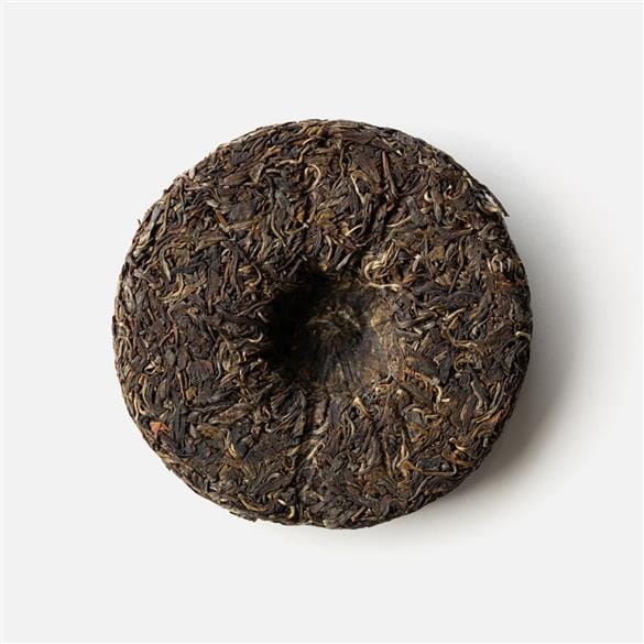 A piece of Kokang Gold Leaf tea cake on a white surface, made by Rishi Tea & Botanicals.