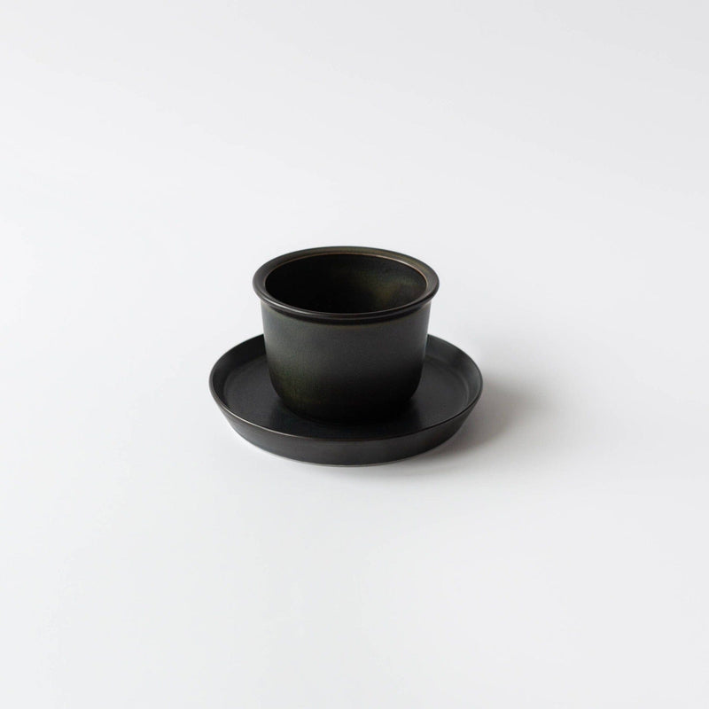 A handcrafted black ceramic cup on a matching saucer from Kinto USA, Inc rests elegantly against a white background, exuding timeless charm.