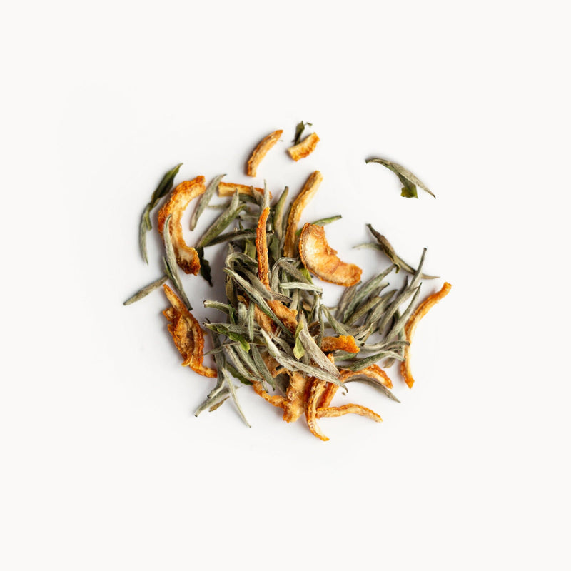 A blend of Rishi Tea & Botanicals dried orange peel and green tea leaves, with a subtle hint of yuzu essence, scattered on a white background.