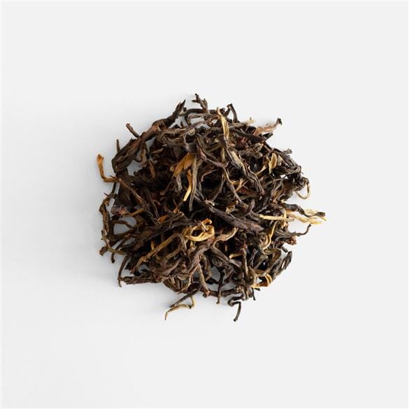 A pile of Rishi Tea & Botanicals Doi Wawee Sun-Dried Red Tea leaves on a white surface.