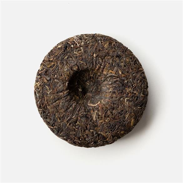 A Doi Wawee Sheng Pu'er Vintage Spring 2020 tea cake on a white surface. (Brand: Rishi Tea & Botanicals)